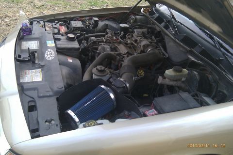 2000 Mercury Grand Marquis - Engine bay of a gold sedan, showing the motor and various components, including an aftermarket air filter.