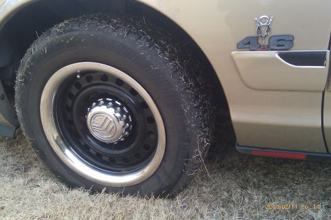 2000 Mercury Grand Marquis - Close-up of a tan car's fender and wheel, a 4.6 badge and a Mercury logo on the hubcap.
