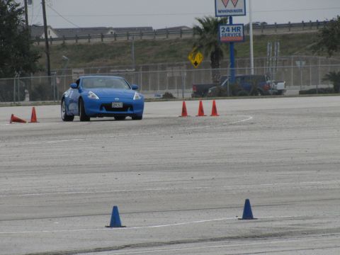 2003 Mazda Protege - A blue sports car is seen on a track, maneuvering around orange cones during what appears to be a driving event.