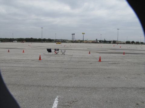 2003 Mazda Protege - An autocross course is set up with orange cones and two chairs on a paved lot under a cloudy sky.