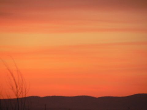 2006 Ford E350 - A vibrant sunset paints the sky with shades of orange and yellow, casting a silhouette over rolling hills and dry grass in the foreground.