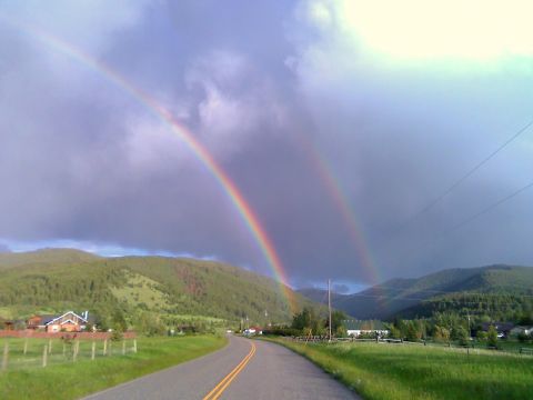 2006 Ford E350 - A double rainbow appears after a storm over a scenic rural road with green hills and scattered houses.