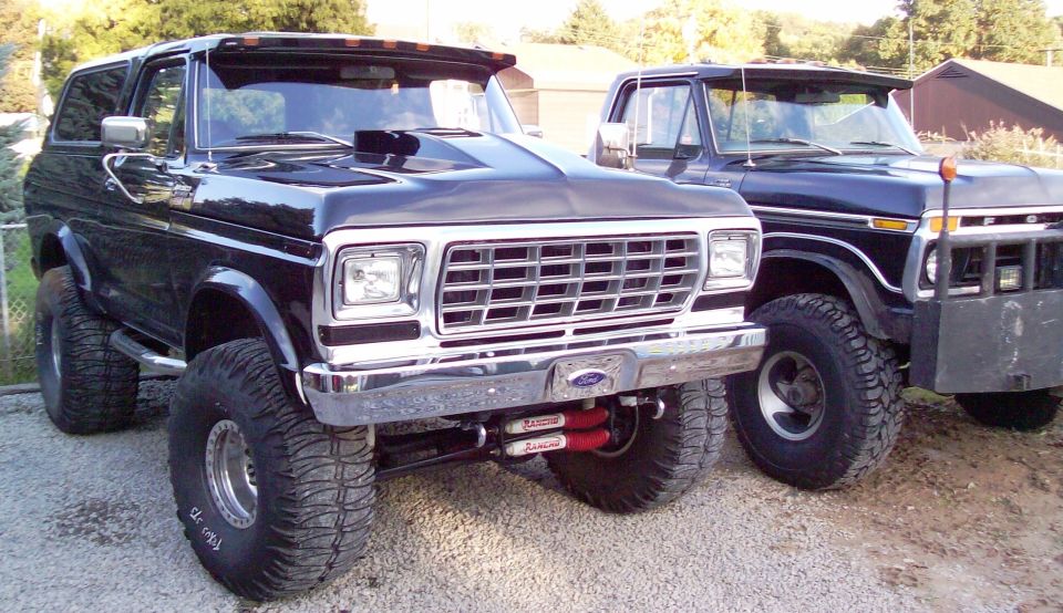 Two black lifted 1978-79 Ford Bronco SUVs with chrome grilles parked outdoors