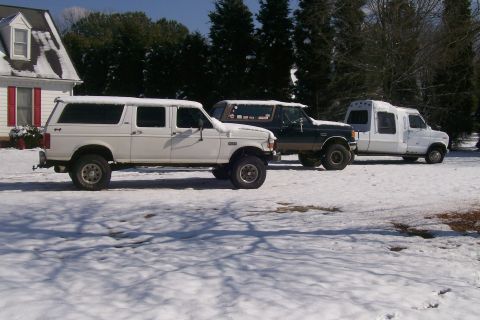1988 Ford Bronco - Three vehicles are parked in a snowy area with a house and trees in the background.