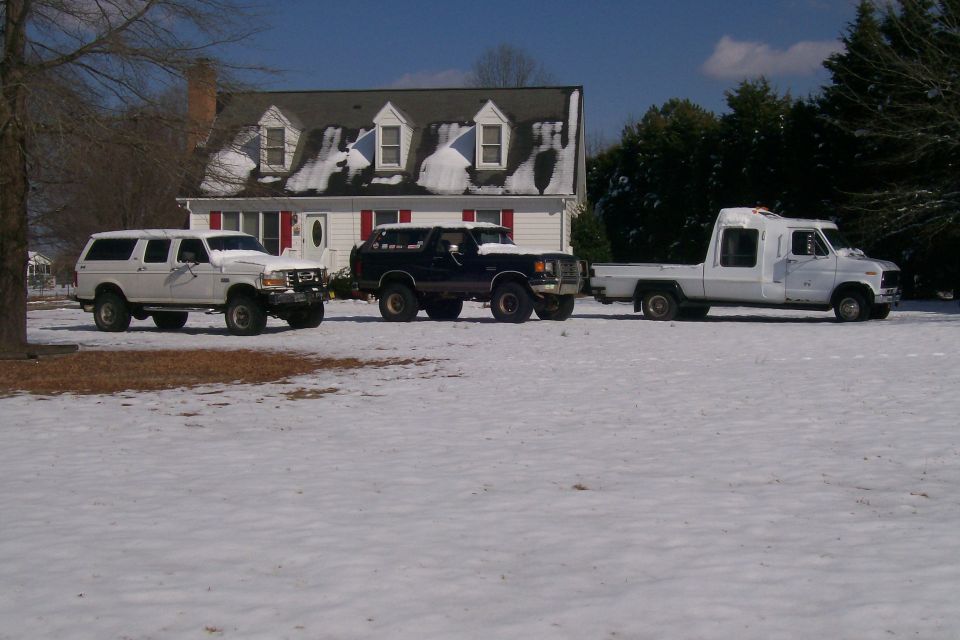 Three trucks parked in a snowy yard in front of a house