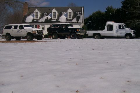 1988 Ford Bronco - Three trucks are parked in the snow in front of a house with snow on the roof.