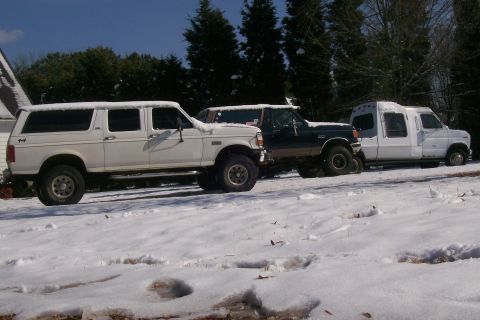 1988 Ford Bronco - Three trucks are parked in a snowy landscape with trees in the background.