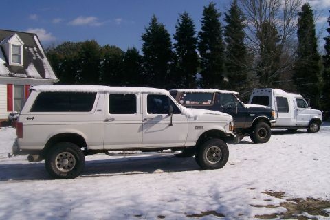 1988 Ford Bronco - Three vehicles, including a white extended cab pickup truck with a camper shell, are parked in the snow.