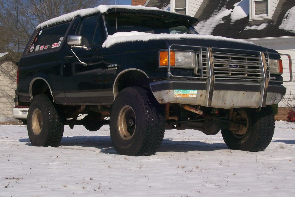 Black lifted Ford Bronco with snow on roof, parked in a snowy yard