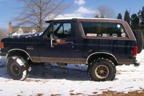 1988 Ford Bronco - A dark blue Ford Bronco with brown trim sits in the snow, equipped with off-road tires and a lifted suspension.