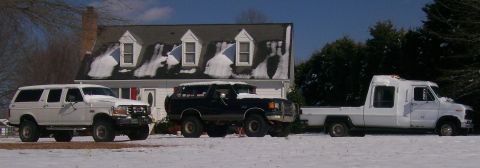 1988 Ford Bronco - Three vehicles sit in a snowy yard in front of a house.