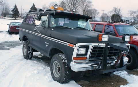 1979 Ford Bronco - A modified Ford Bronco sits in a snowy lot, equipped with auxiliary lights and a front plow.