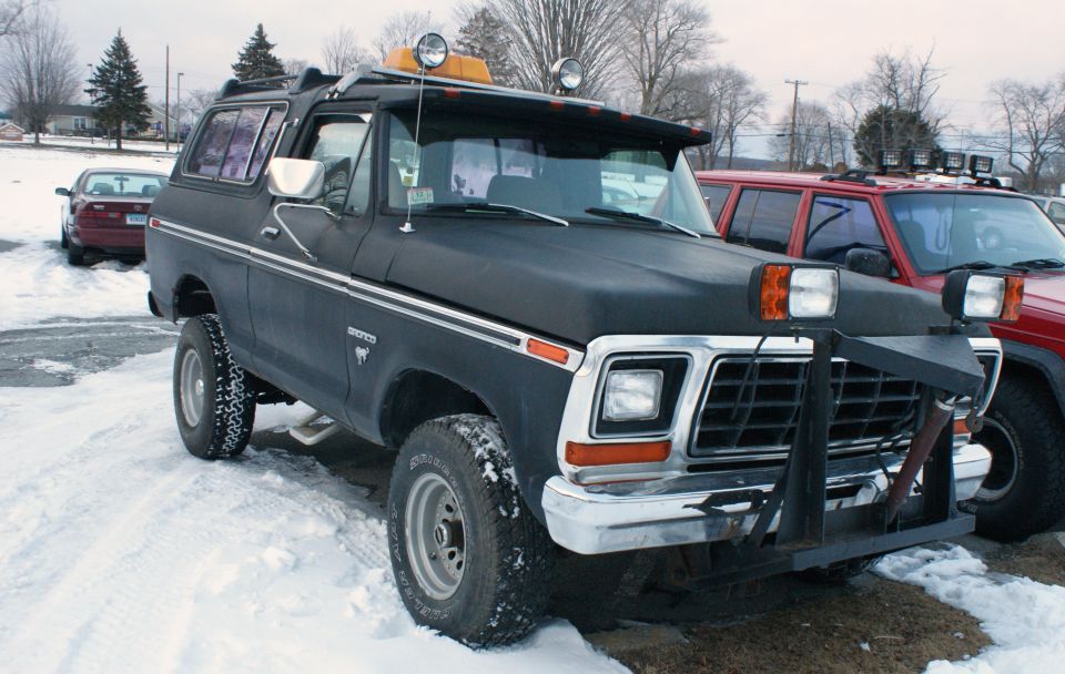 Black Ford Bronco with a plow attachment and roof lights parked in the snow