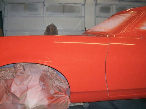 1973 Ford Ranchero - Freshly sprayed bright red body panel, a front fender and door with the wheel opening masked off in crumpled paper, inside a shop with whit…