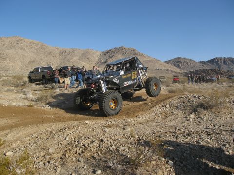 1986 Ford Bronco - A custom off-road buggy navigates a desert course with spectators and other vehicles in the background.