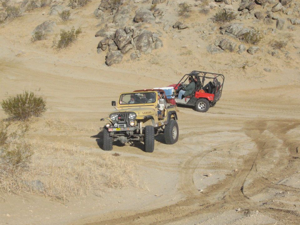 tan Jeep CJ-7 driving on a dirt trail with a red dune buggy behind it