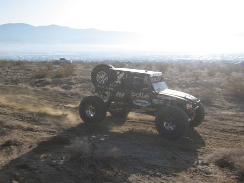 1986 Ford Bronco - A modified off-road buggy navigates a dusty desert terrain, with another vehicle visible in the distance.
