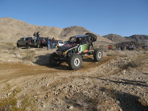 1986 Ford Bronco - Custom off-road buggy navigates a desert trail with spectators and other vehicles present.