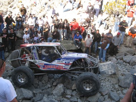 1986 Ford Bronco - A custom off-road buggy, sponsored by Lucas Oil, tackles a rocky course with spectators watching.