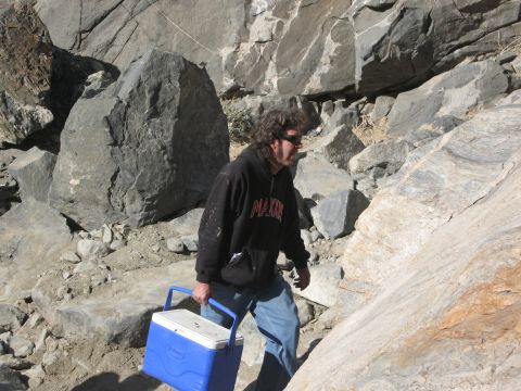 1986 Ford Bronco - Man carries a cooler through a rocky, outdoor terrain. The image includes a 'SUPERMOTORS' watermark.