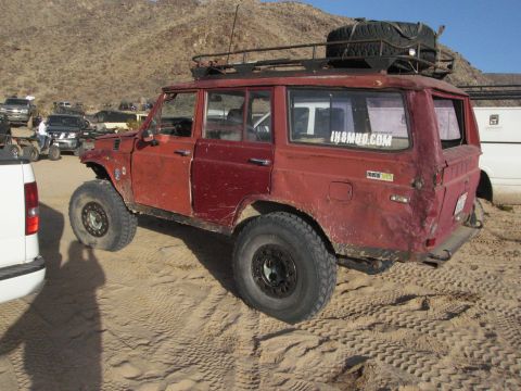 1986 Ford Bronco - This heavily modified SUV is parked in a sandy, desert-like environment with other vehicles visible in the background.