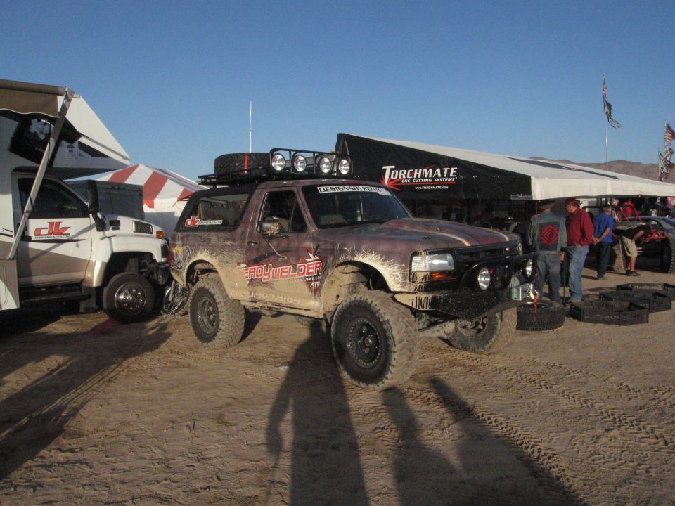 Brown Ford Bronco with roof rack and off-road tires, parked next to an RV