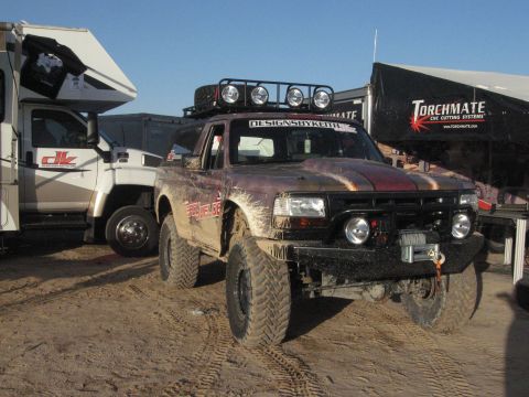 1986 Ford Bronco - Modified pickup truck with off-road tires and winch is parked next to an RV.