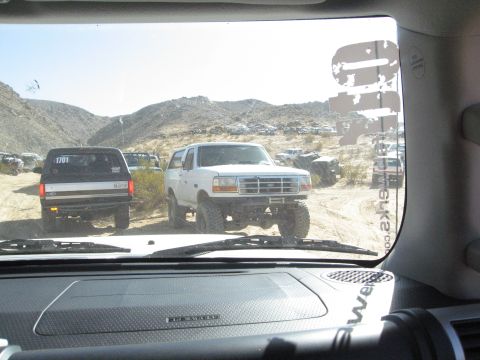 1986 Ford Bronco - A white Ford Bronco is parked on a dirt road in a desert landscape, with other vehicles visible in the distance.