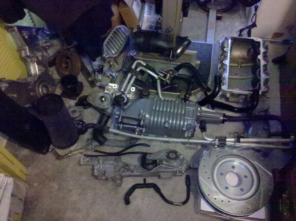Supercharger, brake rotor, air filter, and other engine components scattered on a concrete floor