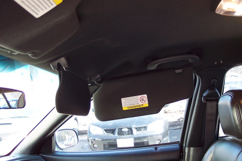Interior view of a car showing sun visors, a rearview mirror, and a dark-colored car visible through the windshield