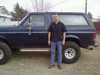 Guy standing next to a dark blue 1987 Ford Bronco
