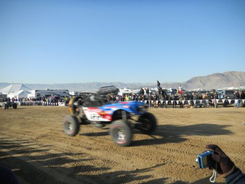 1997 Ford Ranger - A blurred off-road buggy races across a sandy track during an event, with crowds watching in the background.