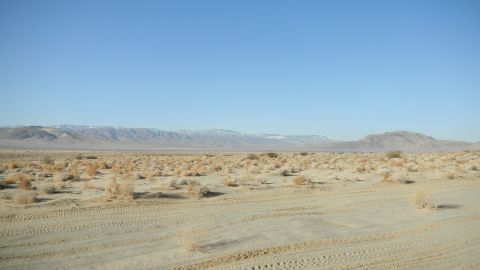 1997 Ford Ranger - A vast desert scene with tire tracks in the foreground and mountains on the horizon under a clear blue sky.