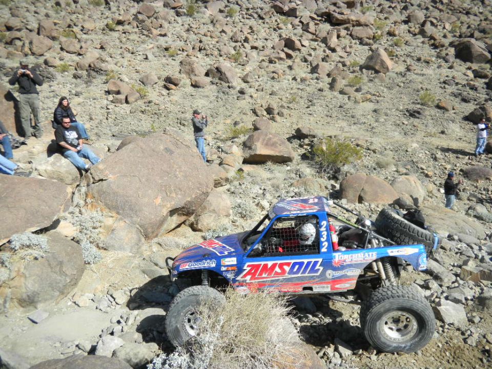Blue off-road race truck with AMSOIL livery navigating rocky terrain
