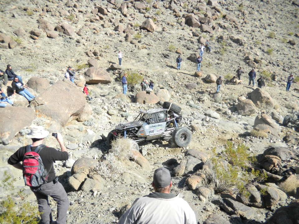 Off-road buggy climbing a rocky hill with spectators watching