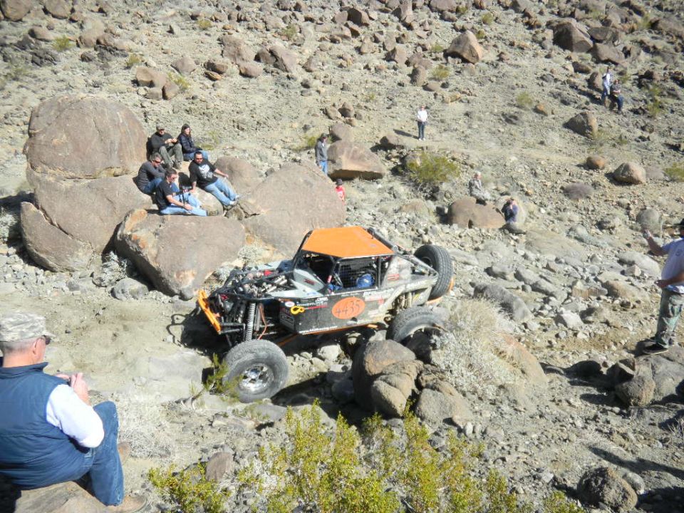 Off-road buggy with orange roof and number 435 on side, navigating rocky terrain