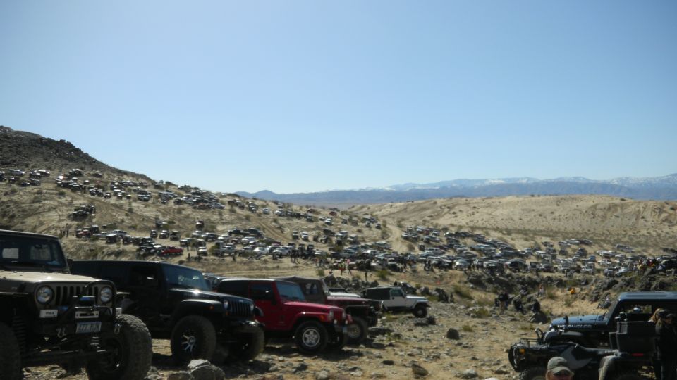 Many off-road vehicles parked on a desert hillside under a clear blue sky