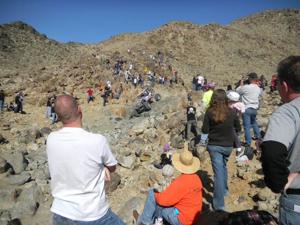 Off-road buggy climbing a rocky hill with spectators watching