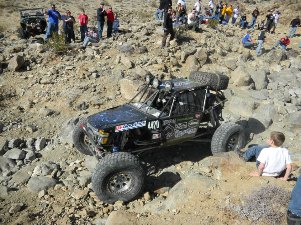 Black off-road buggy with large tires and a roll cage, navigating a rocky terrain