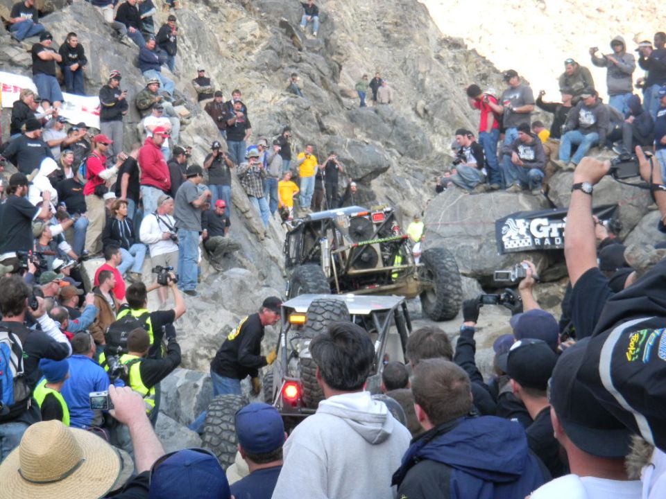 Off-road buggy navigates a steep, rocky incline as a crowd watches from the hillside