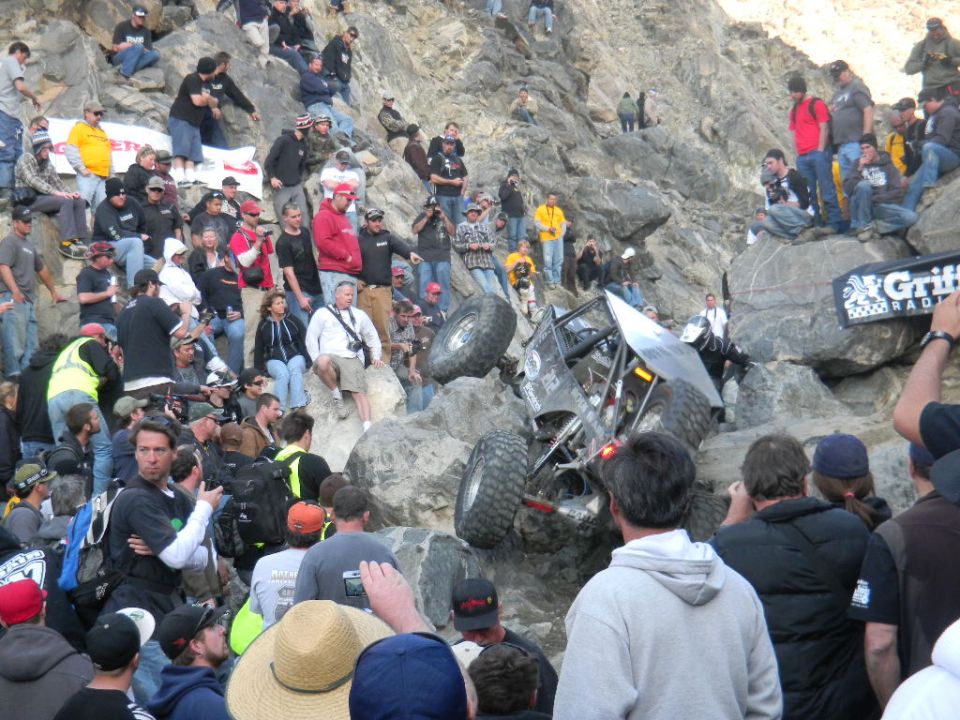 Off-road buggy climbing a steep, rocky incline with a crowd watching