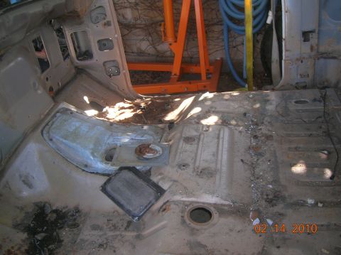 1985 Ford Bronco - The interior of a vehicle is shown stripped down to its metal floor pans, with an engine hoist visible behind it.