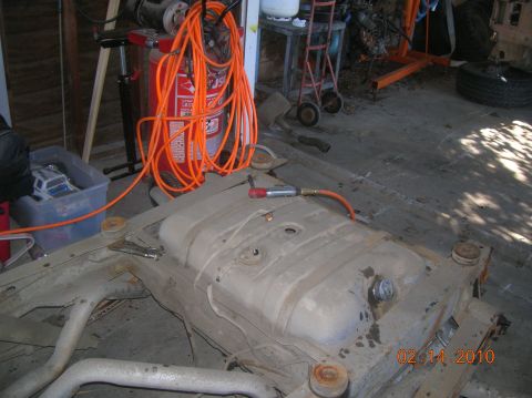 1985 Ford Bronco - Fuel tank and frame assembly in a workshop setting with tools and equipment.