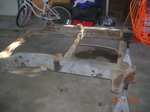 1985 Ford Bronco - A rusty vehicle frame sits on jack stands in a garage, with a bicycle visible in the background.