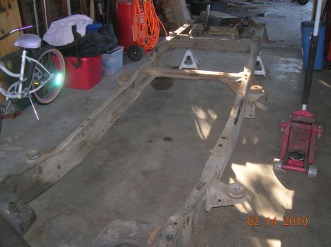 1985 Ford Bronco - A vehicle frame is shown on jack stands in a garage, with a bicycle and tools visible in the background.