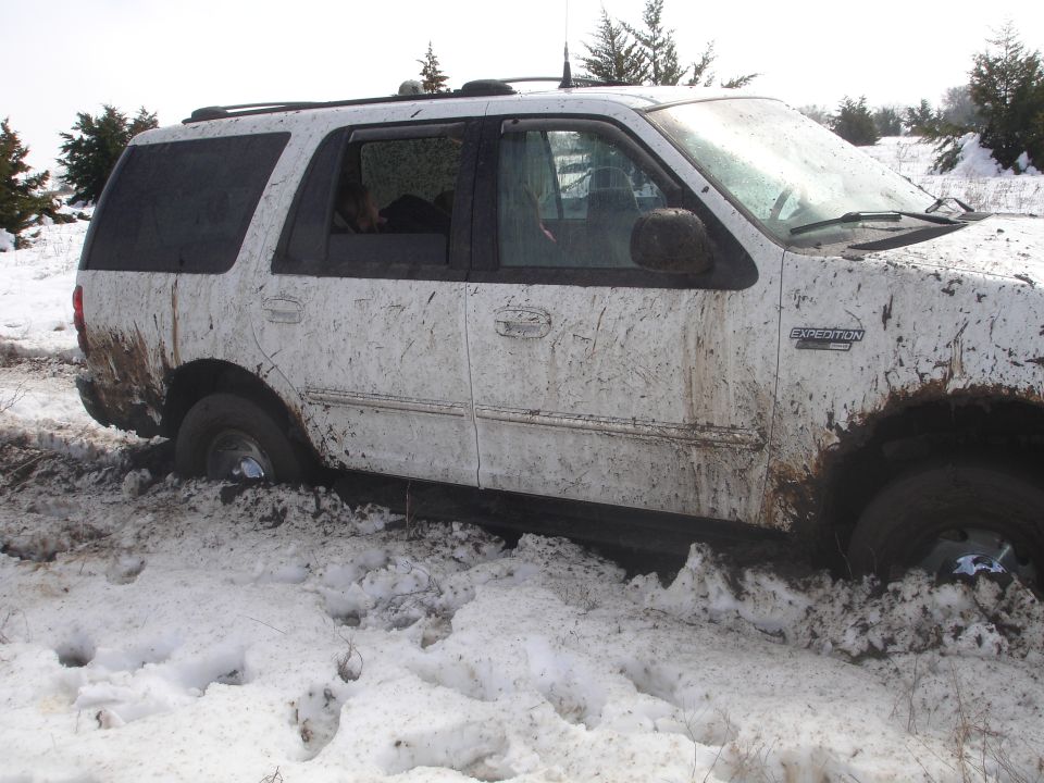 White 2002 Ford Expedition covered in mud and snow, stuck in a snowy ditch