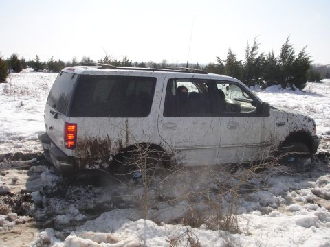 2002 Ford Expedition - A white 2002 Ford Expedition is stuck in a muddy, snowy field, with its tires deep in the mire.