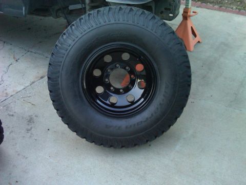 1986 Ford Bronco - A close-up view of a black tire and wheel assembly resting on a concrete surface.