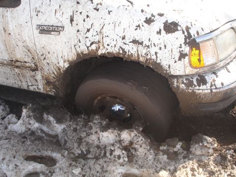 2002 Ford Expedition - A white 2002 Ford Expedition is stuck in mud and snow, with its front wheel submerged.