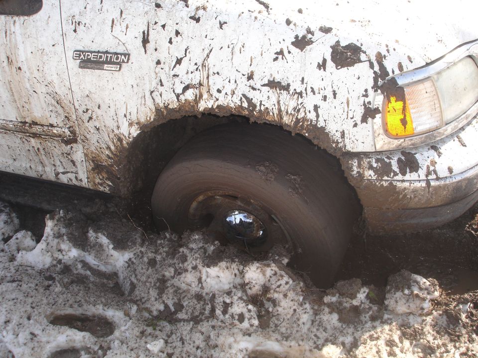 White 2002 Ford Expedition stuck in mud and snow, front wheel deep in muck